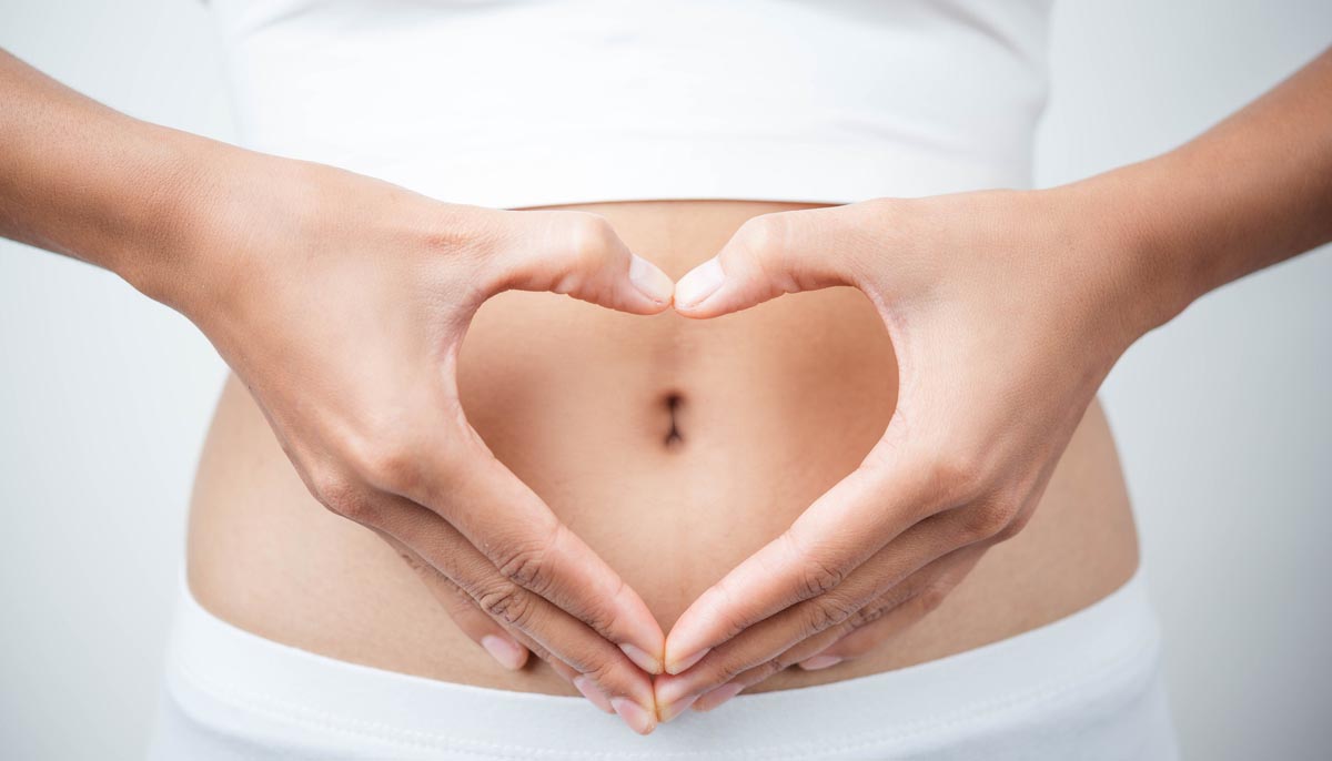 A woman holds her hands over her stomach in the shape of a heart